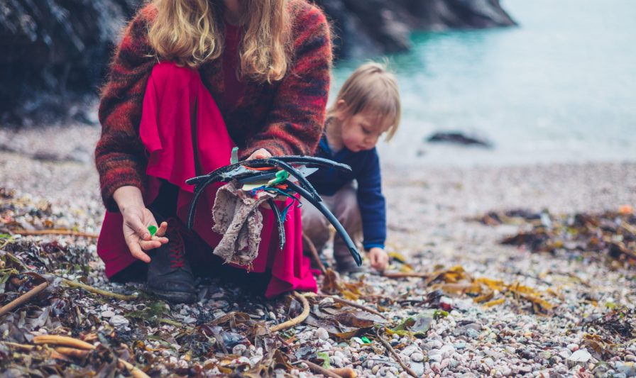 A little toddler is helping his mother clean up plastic rubbish on the beach