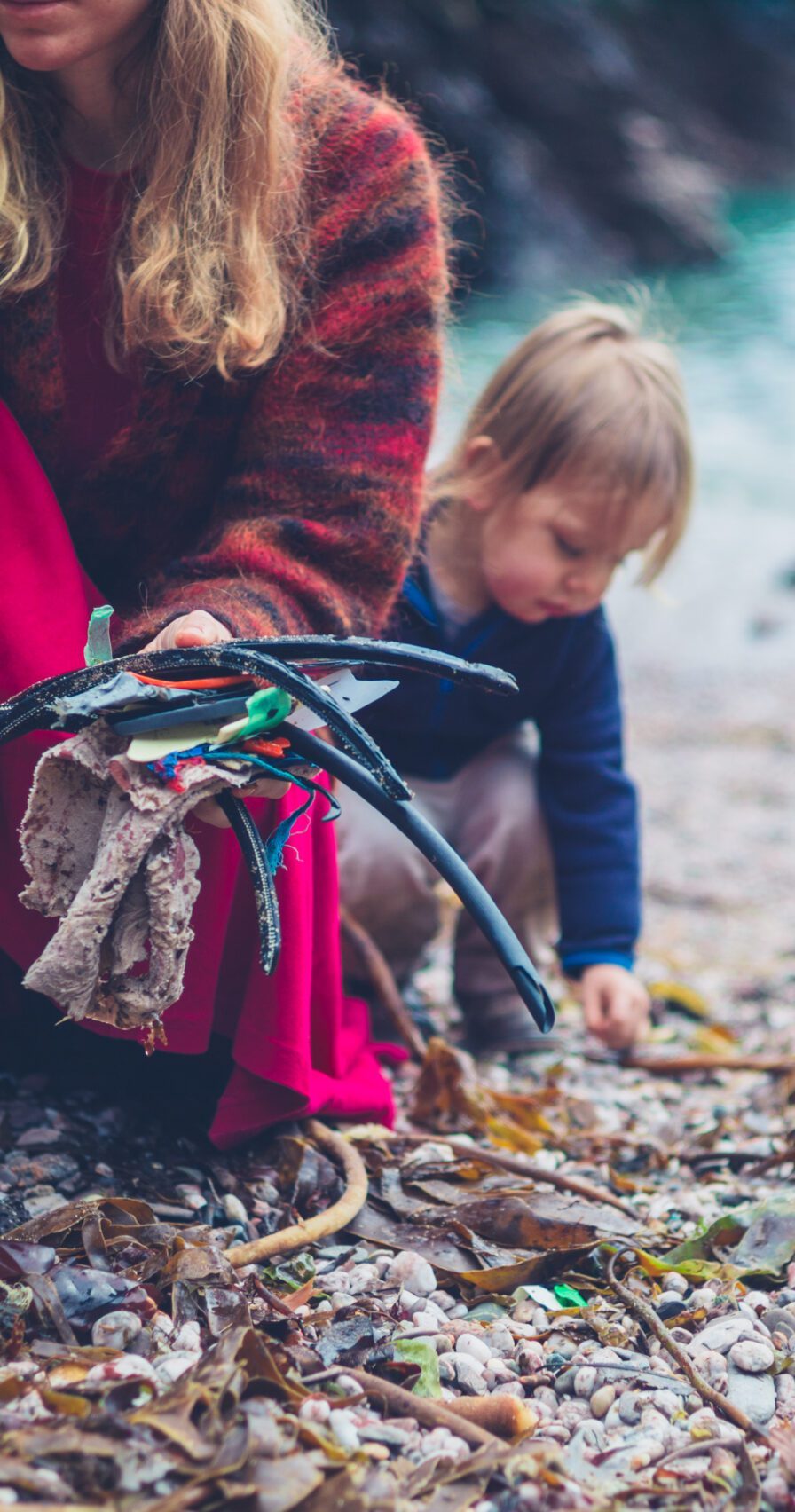 A little toddler is helping his mother clean up plastic rubbish on the beach