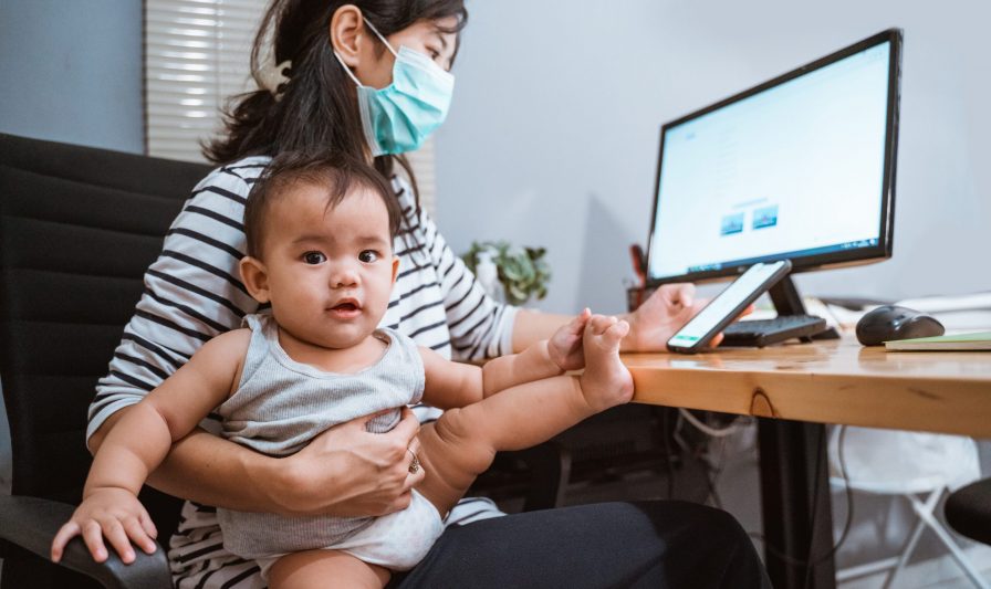 mother with masks working from home while baby sitting